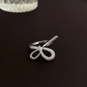 Macro view of silver bow-shaped open ring with cubic zirconia on black leather surface