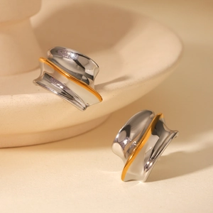Close-up of two-tone gold and silver earrings with an irregular wavy surface design