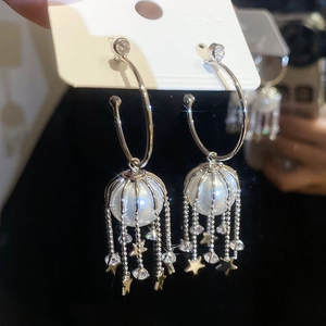 Detail view of silver C-shape earrings with hanging pearls, stars, and crystal tassels