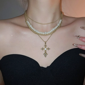 Detail of layered gold necklace with pearl strands and crystal cross pendant on neck