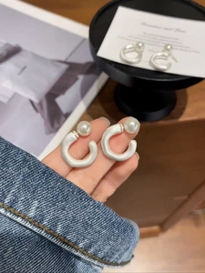 Macro detail of French style matte pearl C-shaped earrings held in hand for close-up view