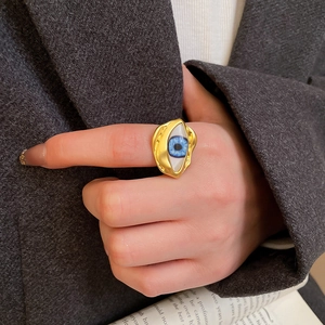 Detailansicht eines klobigen goldenen Evil Eye Rings am Zeigefinger mit blauem Auge