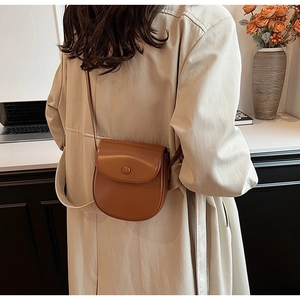 Braune matte Satteltasche aus Leder an Model in hellem apricotfarbenem Trenchcoat