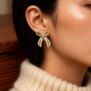 Detail showing a gold-plated bow earring with white zircon inlay on model's ear