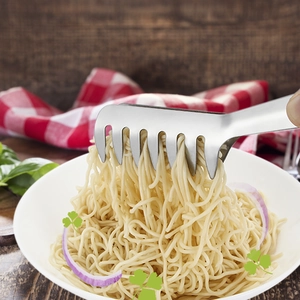 Stainless steel pasta tongs picking up noodles over a bowl on a wooden table