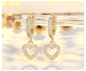 Macro shot of gold heart dangle earrings with white cubic zirconia pavé on a stand