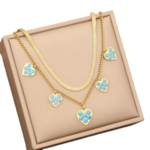 Golden double-layer necklace with heart charms and blue evil eye patterns in a beige box