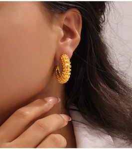 Macro detail of gold-plated C-shaped earrings with textured beaded surface on a model