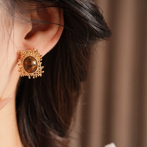 Close-up of gold lattice woven earrings with oval tiger eye stone on a model ear