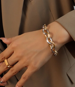 Close-up of gold and silver tone link bracelet on wrist with khaki blazer background