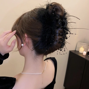 Detail view of a black feather hair claw clip with beads on a model's hair