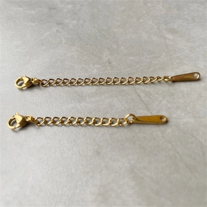 Detail of gold stainless steel extension chains with lobster clasps on marble background