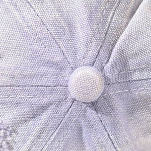 Macro detail of the light purple twill fabric and reinforced stitching on the baseball cap
