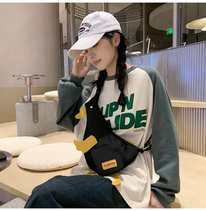 Close-up of a black canvas duck-shaped crossbody bag worn by a model in a cafe setting