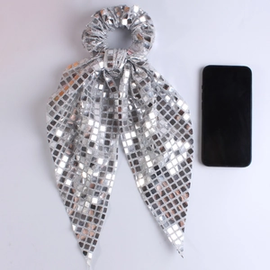 Close-up of shiny silver sequined scrunchie with long bow beside a smartphone for size