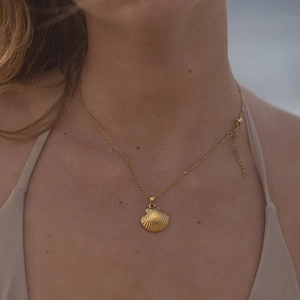 Detailed close-up of a golden seashell pendant necklace worn on a model's neck area