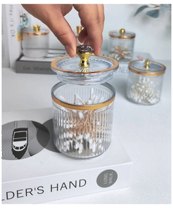 Lifting the lid of a clear striped storage jar with gold trim and diamond handle