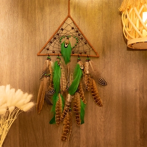 Triangle dream catcher wall hanging with green feathers on a rustic wood background