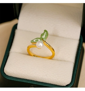 Macro shot of gold pearl ring with green enamel leaves on a jewelry box cushion
