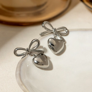 Macro view of silver bow and heart pendant earring with mirror polished surface
