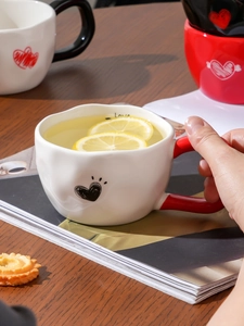 Close-up of a white ceramic mug with red handle, heart patterns and lemon tea inside