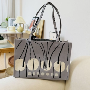 Close-up of gray knitted tote bag with black lines and white dot pattern on a soft sofa