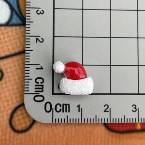 Close-up of a miniature resin Christmas hat next to a ruler showing its 1.5cm size