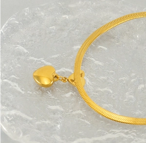 Macro shot of polished gold-plated heart pendant on a flat snake bone chain necklace