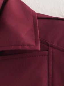 Détail macro de la veste bordeaux montrant le col montant et les coutures en tissu tissé