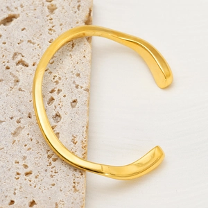 Detailed close-up of a 18K gold plated irregular wave bangle on a stone pedestal