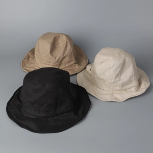 Flat lay detail showing natural linen cotton fabric texture of three bucket hats in basic colors