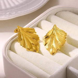 Macro view of golden leaf earrings with detailed metal texture in a white jewelry box