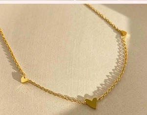 Primer plano de collar de oro con múltiples mini colgantes de corazón sobre textura fina