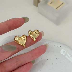 Close-up of golden irregular heart earrings with lava texture shown on fingertips