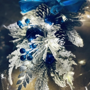 Detailed close-up of snowy pine cones, blue ornaments, and warm LED lights on a garland