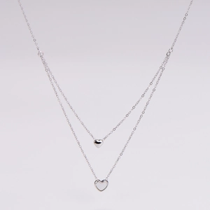 Detail of silver double-layered necklace with solid and hollow heart-shaped pendants