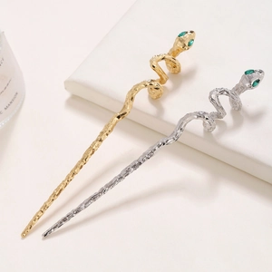 Close-up of gold and silver snake hairpins with scale texture and green stone eyes