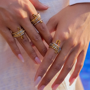 Close-up of stacked gold and silver metal rings with safety pin design and pavé detail