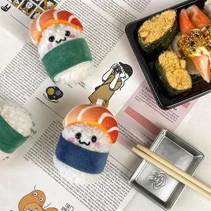 Cute sushi-style plush keychain pendants in three colors displayed on a newspaper background