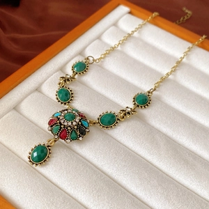 Detail of vintage gold necklace with colorful crystals and green gemstone in a jewelry box