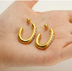 Detail of gold U-shaped hoop earrings with five inlaid white pearls held in hand