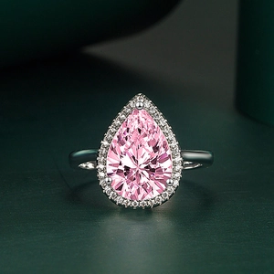 Close-up of pear-cut pink gemstone ring with white crystals on a green background