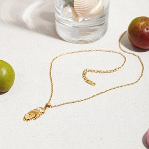Détail d'un pendentif palmier en or 18k avec perles sur fond de plage d'été