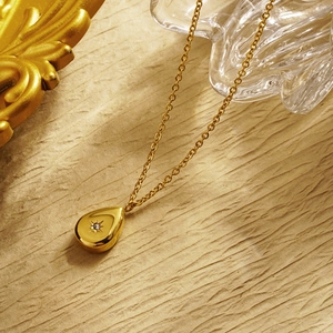 Close-up of gold water-drop pendant with starburst engraving and sparkling zircon stone
