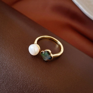 Detailansicht eines Goldrings mit weißer Perle und dunklem Perlmutt-Kleeblatt
