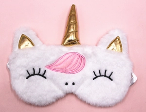 Detail of plush white unicorn sleep mask with golden horn and pink mane on pink background