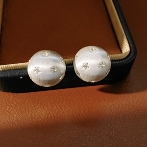 Vue macro montrant la texture du métal brossé et les montures étoilées de ces boucles d'oreilles