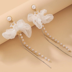 Détail de boucles d'oreilles à pompons perles avec nœud en dentelle et chaîne dorée