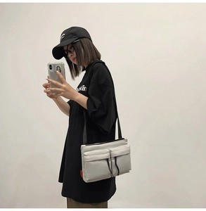 Detail of light grey nylon messenger bag with double front pockets and black zippers