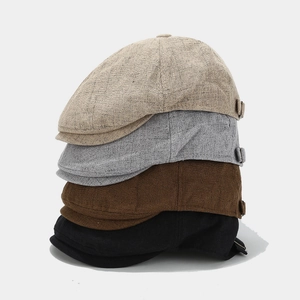 Vertical stack of linen newsboy caps in beige grey brown and black showing fabric texture
